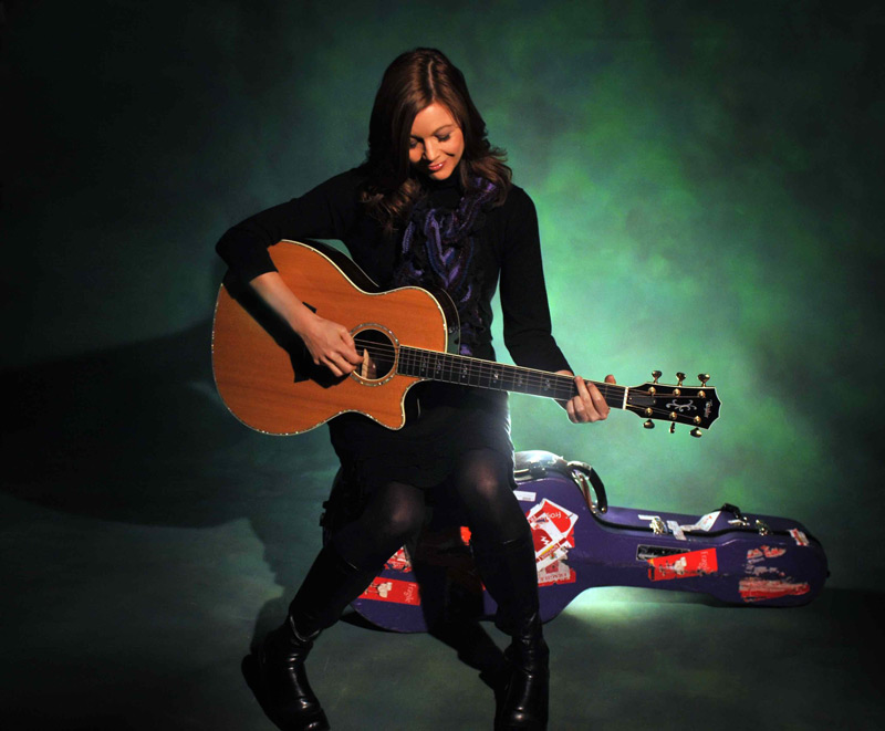 Woman seated on her guitar case playing her guitar