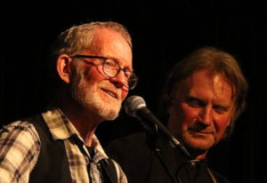 Two men signing into a microphone and playing guitars