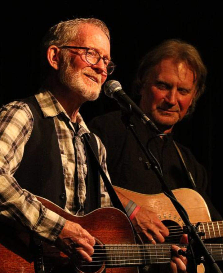 Two men signing into a microphone and playing guitars