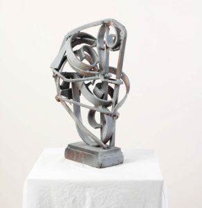 Gray metal sculpture of swirls on a white pedestal