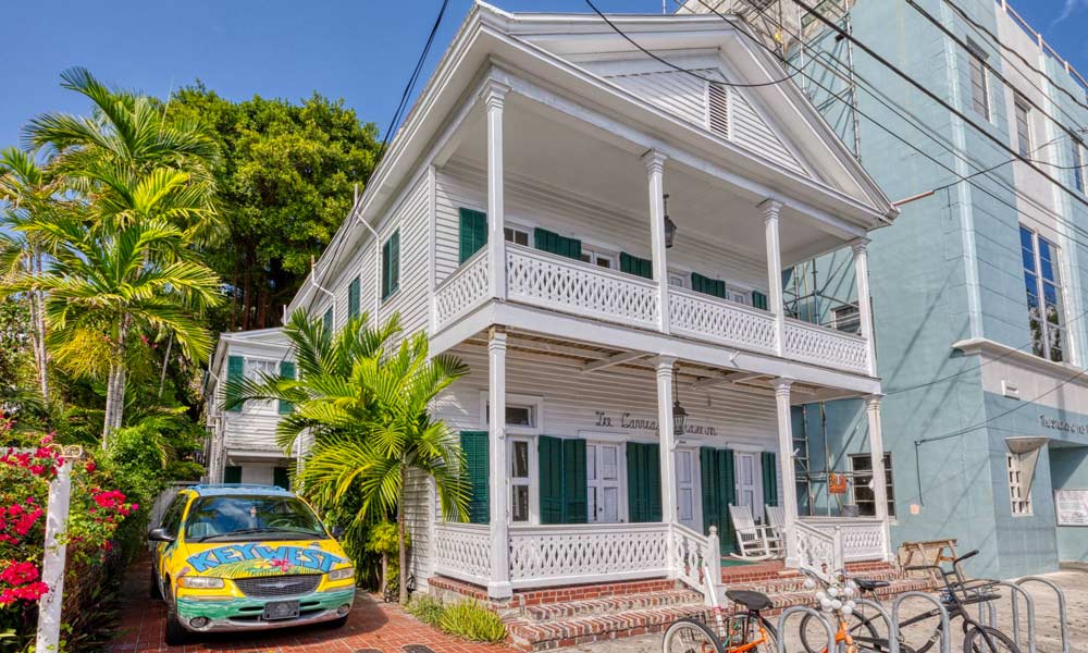 White 2 story house with Key West painted Van in the parking space, bike rack out front with bikes attached