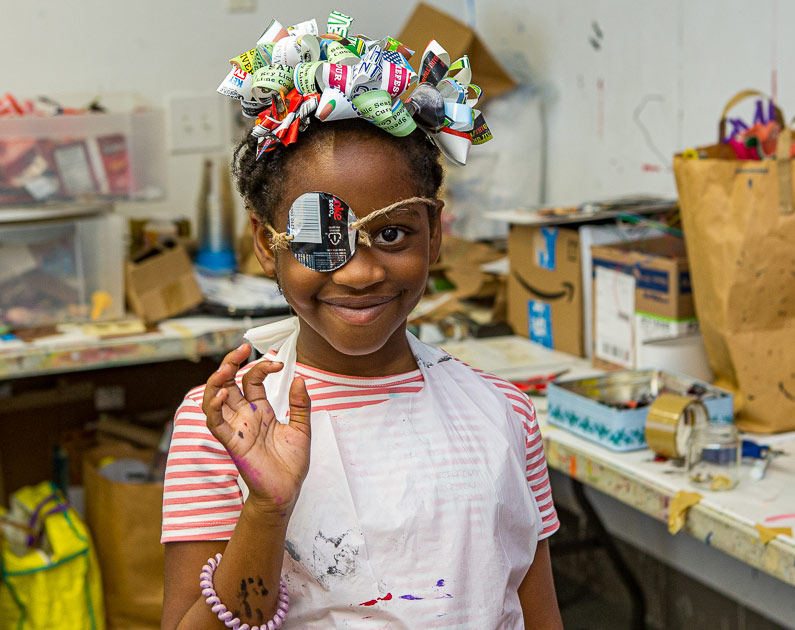 young girl wearing a recycled bow and eye wear smiling and waving at the camera