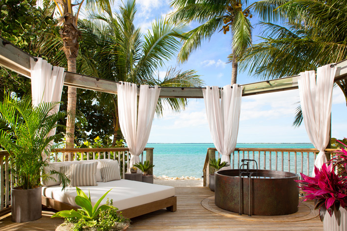 photo of outdoor deck with lounge and hot tube in tropical setting with palms and beach with turquoise water beyond