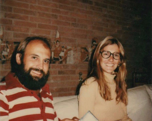 Photograph of man with beard and woman with long hair and glasses sitting on a couch