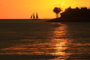 Photo of a sunset off Key West, showing the silhouette of Sunset Key and a sailboat