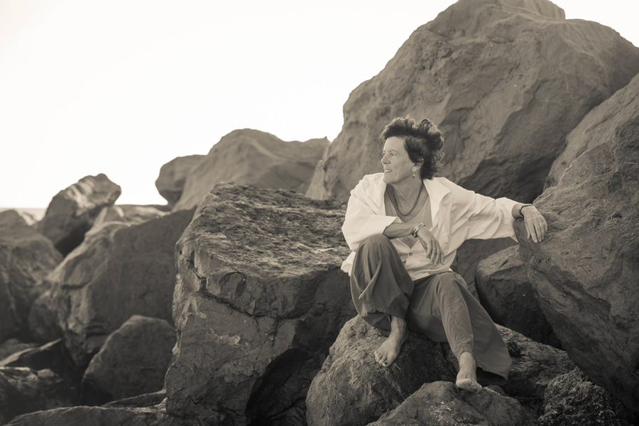 Black and white sepia tone portrait of a woman sitting on rocks in a white flowing shirt