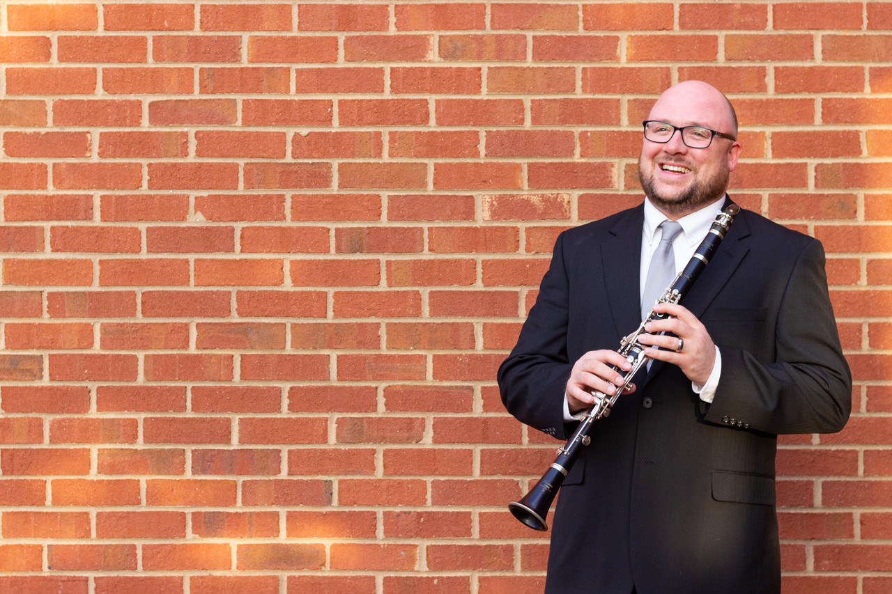Man in suit holding a clarinet in front of a brick wall.