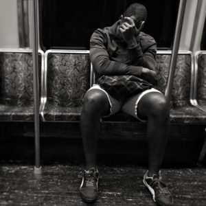 Black and white image of a man asleep with his face in his hand, seated on a train.