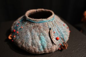 A felt vessel with small opening at top with red beads and strings.