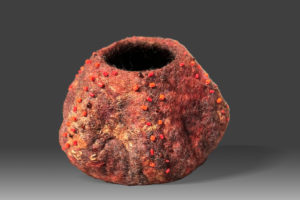 Red and orange wet-felted wool vessel with opening at the top and added beading.