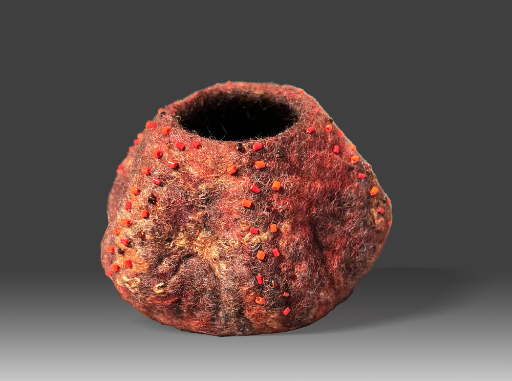 Red and orange wet-felted wool vessel with opening at the top and added beading.