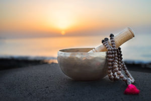 wooden beaded mala necklace wrapped around a mortar and pestle with a sunset in the background