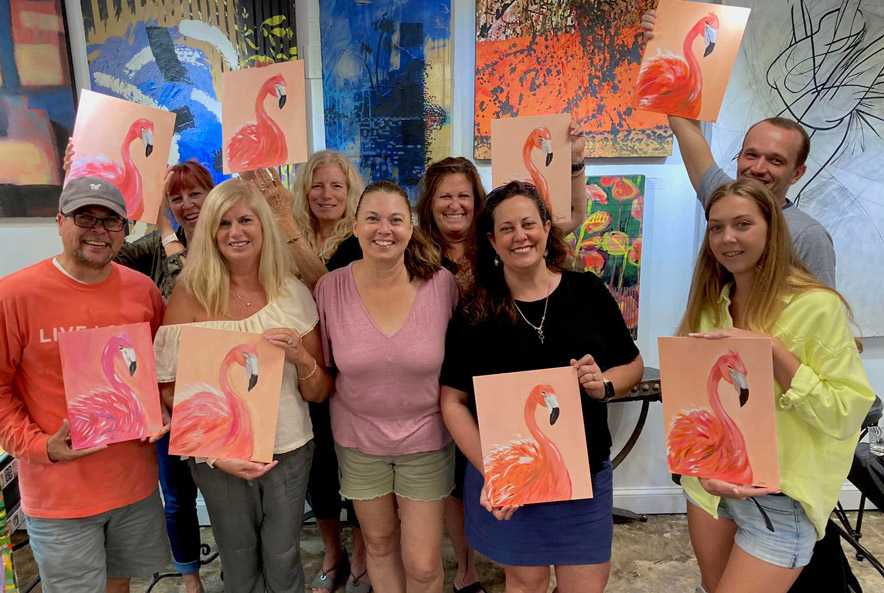 Group of people holding paintings of flamingos in a painting class.
