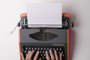 Hands hovering over a typewriter with black keys and orange cover.