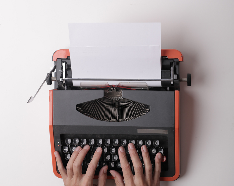 Hands hovering over a typewriter with black keys and orange cover.