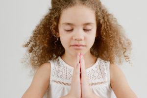 Young mixed race girl with curly hair in the praying yoga pose with eyes closed.