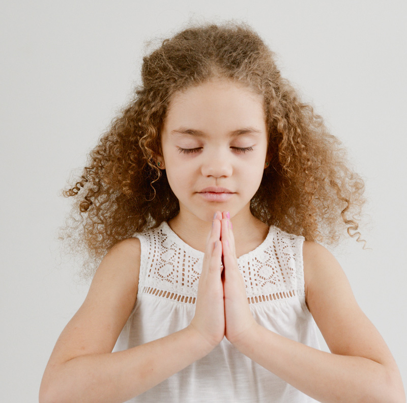 Young mixed race girl with curly hair in the praying yoga pose with eyes closed.