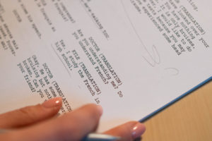 Image of a printed screenplay with a hand holding a pen making edits.