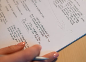 Image of a printed screenplay with a hand holding a pen making edits.