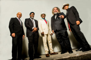 Quintet of male musicians in suits taken from ankle-height looking up.