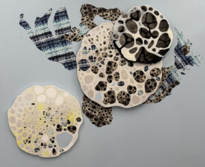 Layered biomorphic shapes with spotted textures in black, cream, and blue, arranged like cellular structures on a pale background.