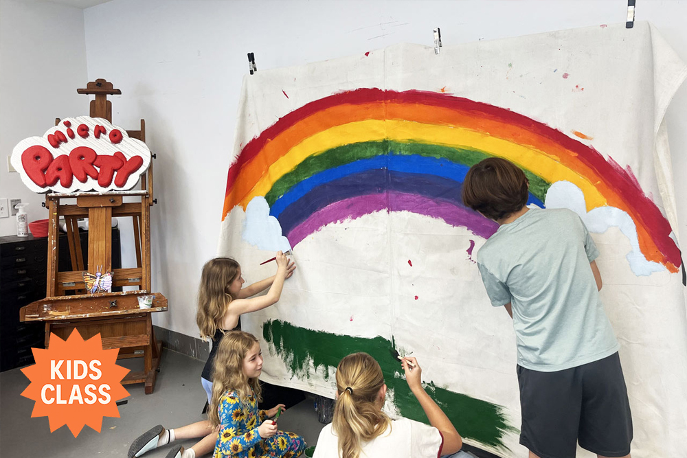 A group of children work together to paint a large rainbow mural on a wall-sized canvas in a studio. A bright orange badge in the corner reads “Kids Class.”