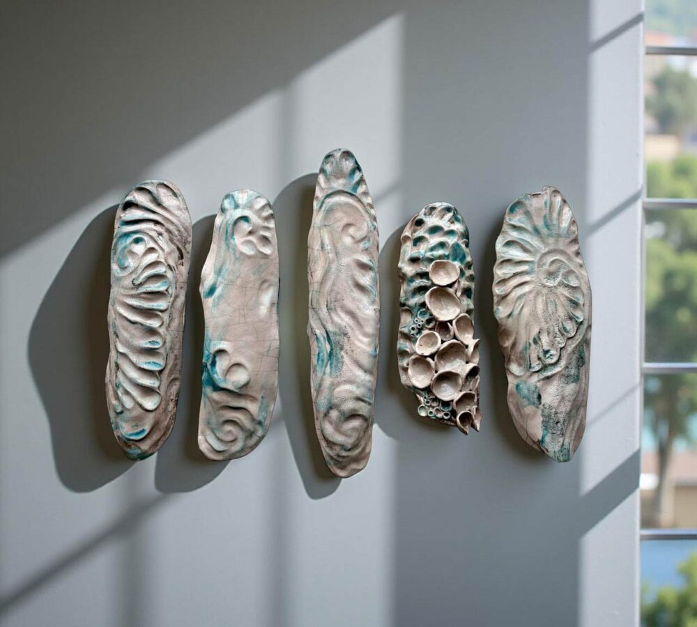 Five elongated ceramic pieces mounted on a wall, textured with wave-like and coral-like patterns in cream and turquoise tones.