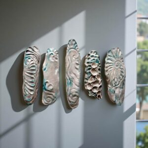 Five elongated ceramic pieces mounted on a wall, textured with wave-like and coral-like patterns in cream and turquoise tones.