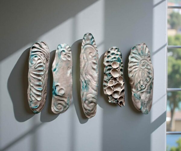 tracey-delellis Five elongated ceramic pieces mounted on a wall, textured with wave-like and coral-like patterns in cream and turquoise tones.