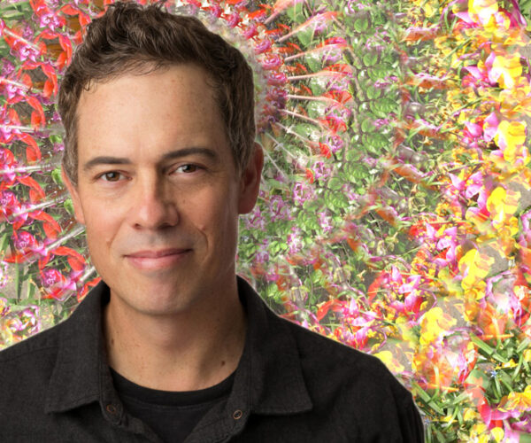 Eric_Dyer-headshot-2021-wBG Artist Eric Dyer portrait in front of a vibrant kaleidoscopic floral background, highlighting his experimental visual art style.