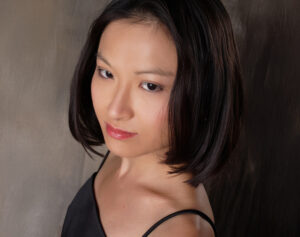 Portrait of May Phang, pianist, with short black hair, wearing a black spaghetti strap top, looking directly at the camera with a neutral expression.
