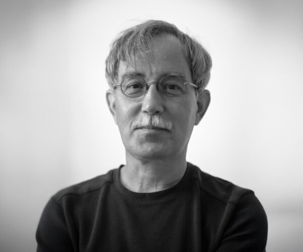 gd.by.DL Black-and-white portrait of author Gordon Dahlquist wearing glasses and a dark shirt, facing the camera with a calm expression against a softly blurred background.