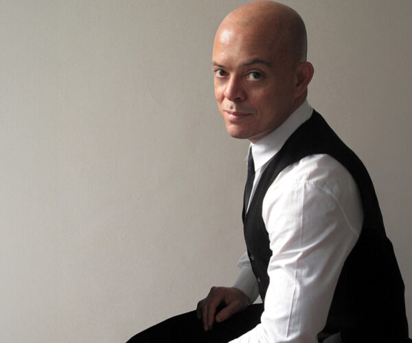 sergio Portrait of Sergio Baradat, seated against a plain wall, wearing a white shirt, black vest, and tie, looking at the camera with a slight smile.
