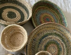 A collection of handwoven baskets in natural and muted tones of beige, green, and multicolor, arranged on a light cloth background.