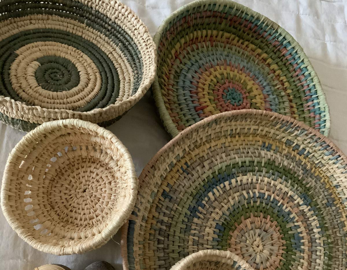 baskets A collection of handwoven baskets in natural and muted tones of beige, green, and multicolor, arranged on a light cloth background.