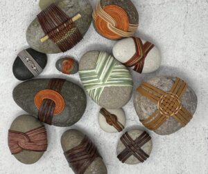 Collection of smooth river stones wrapped with colorful leather and cord in decorative woven patterns.