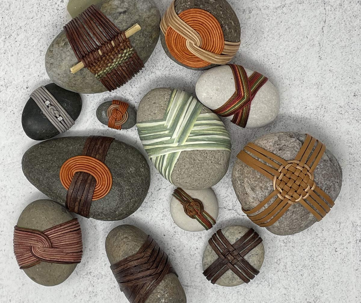 botto-rock-wrapping Collection of smooth river stones wrapped with colorful leather and cord in decorative woven patterns.