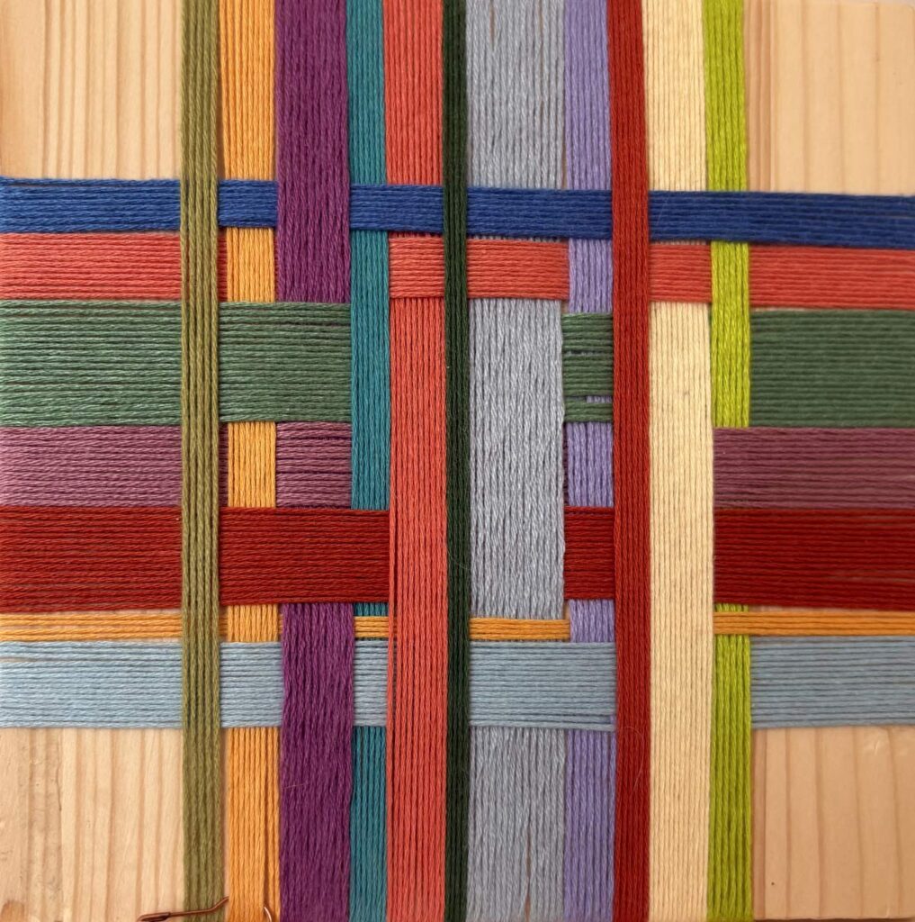 Close-up of multicolored yarn woven in a geometric pattern on a wooden board.