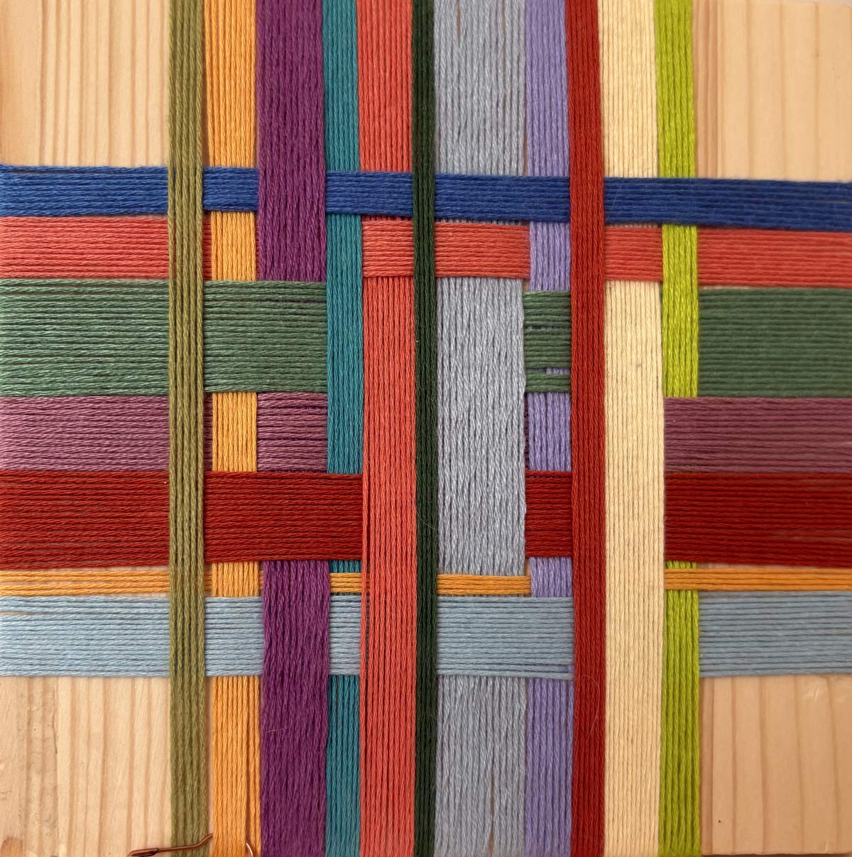 Close-up of multicolored yarn woven in a geometric pattern on a wooden board.