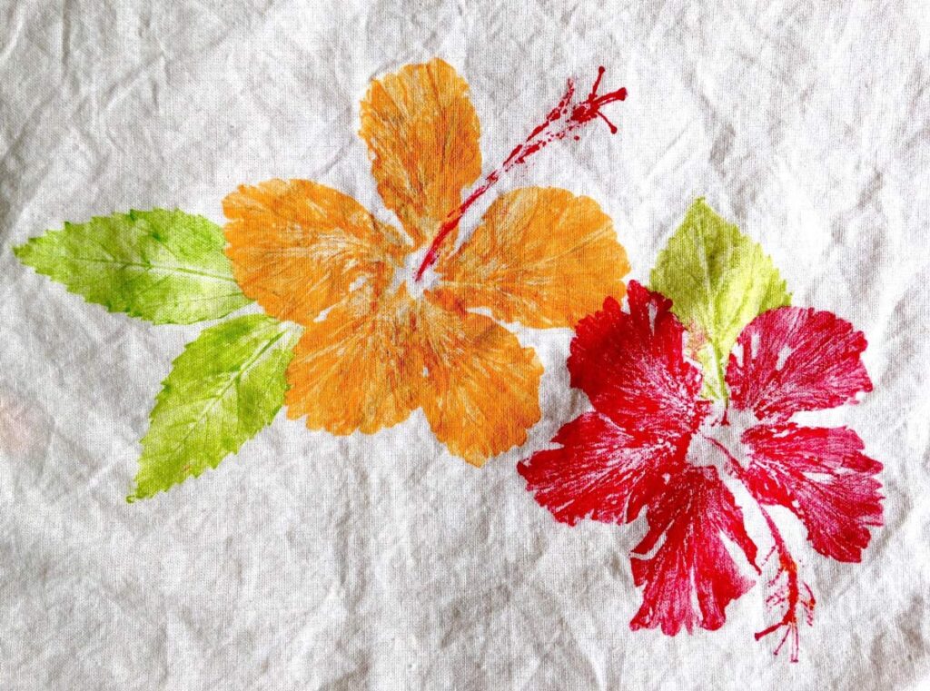 Two brightly colored hibiscus flower prints—one orange, one red—on white fabric, accented by green leaves.