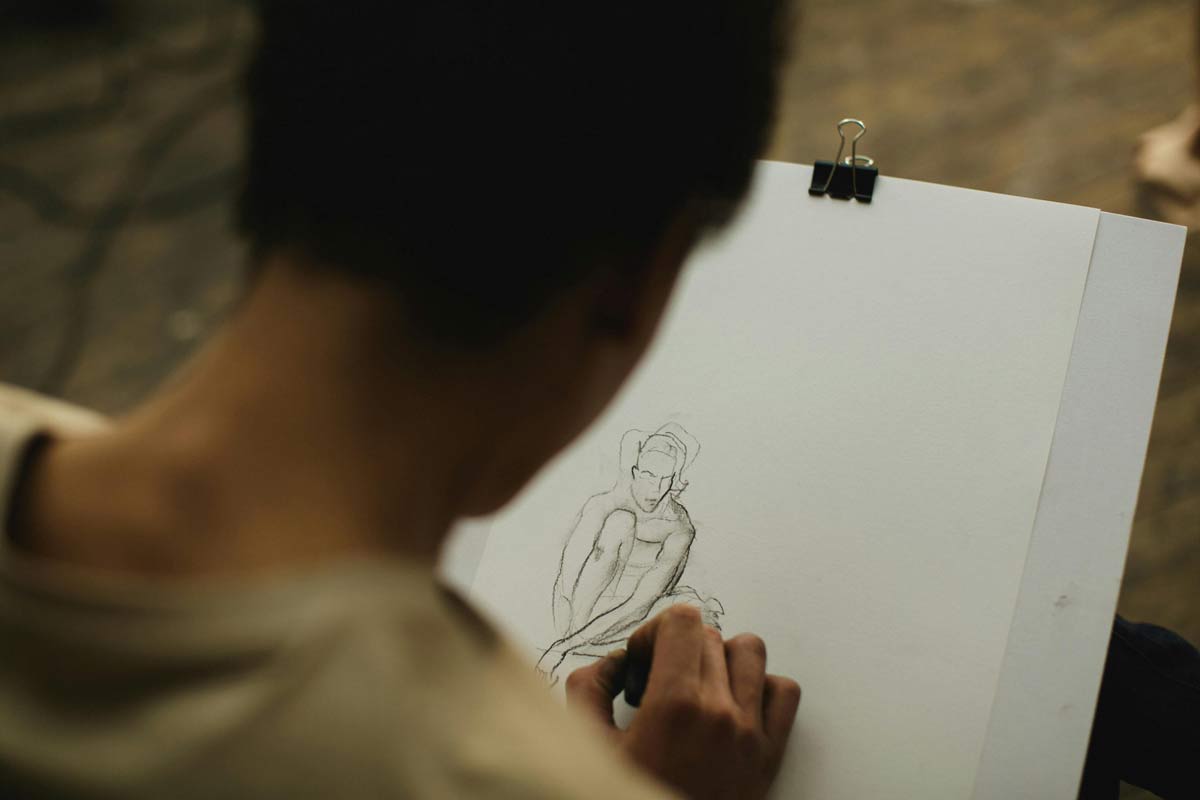 figure-drawing Artist sketching a seated human figure in pencil on a white pad.