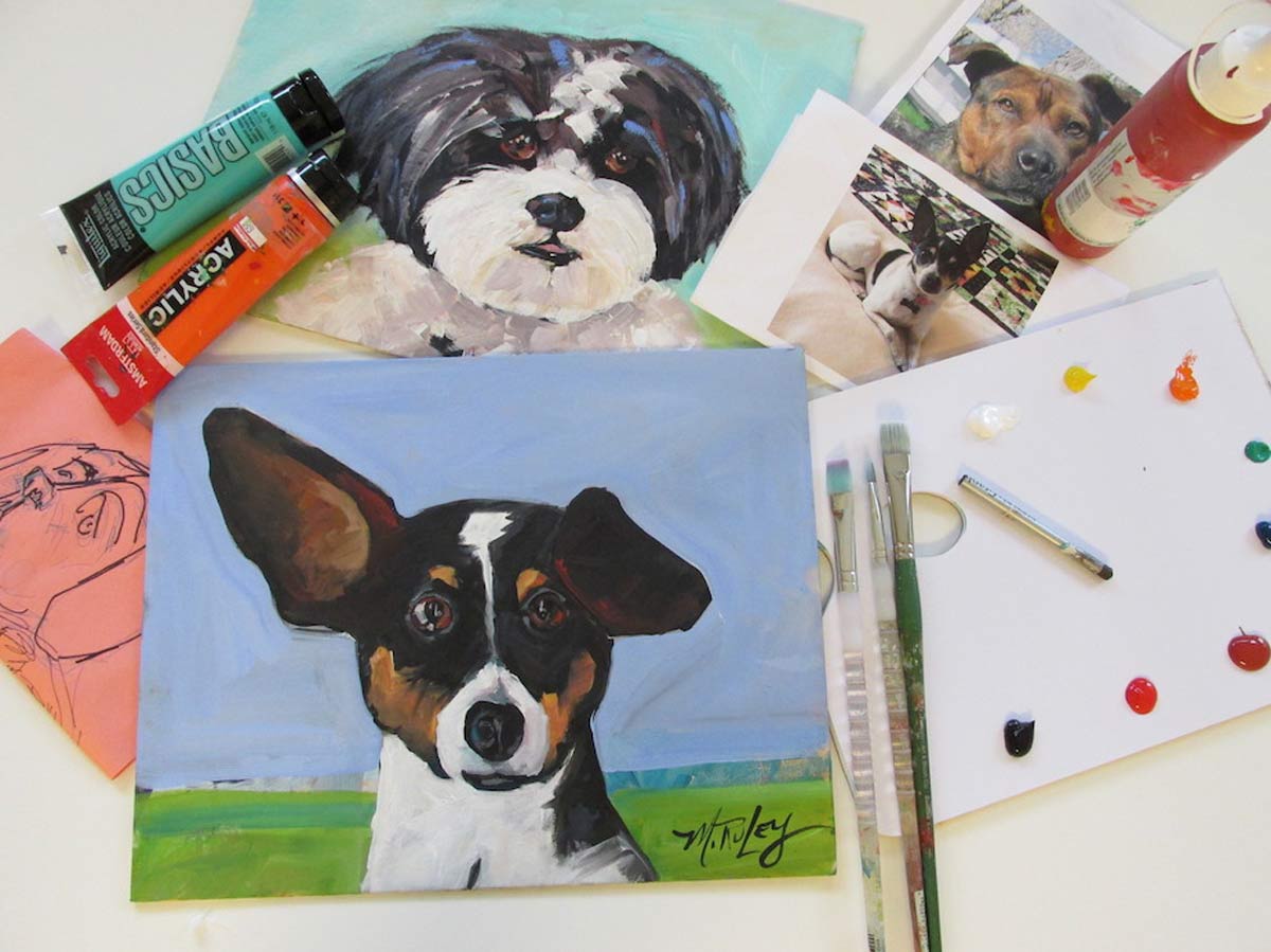 maggie-ruley---pet-portrait-class-promo1-sm Acrylic paintings of dogs surrounded by art supplies, paint tubes, and brushes on a white table.