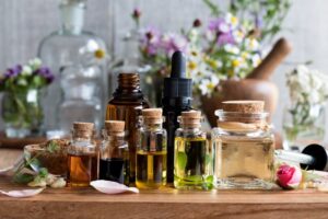 Assortment of glass bottles filled with oils and herbs on a wooden table, surrounded by flowers and petals.