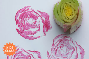 A cut celery stalk dipped in pink paint creates rose-like prints on white paper, demonstrating a simple and colorful nature-based art technique for kids.