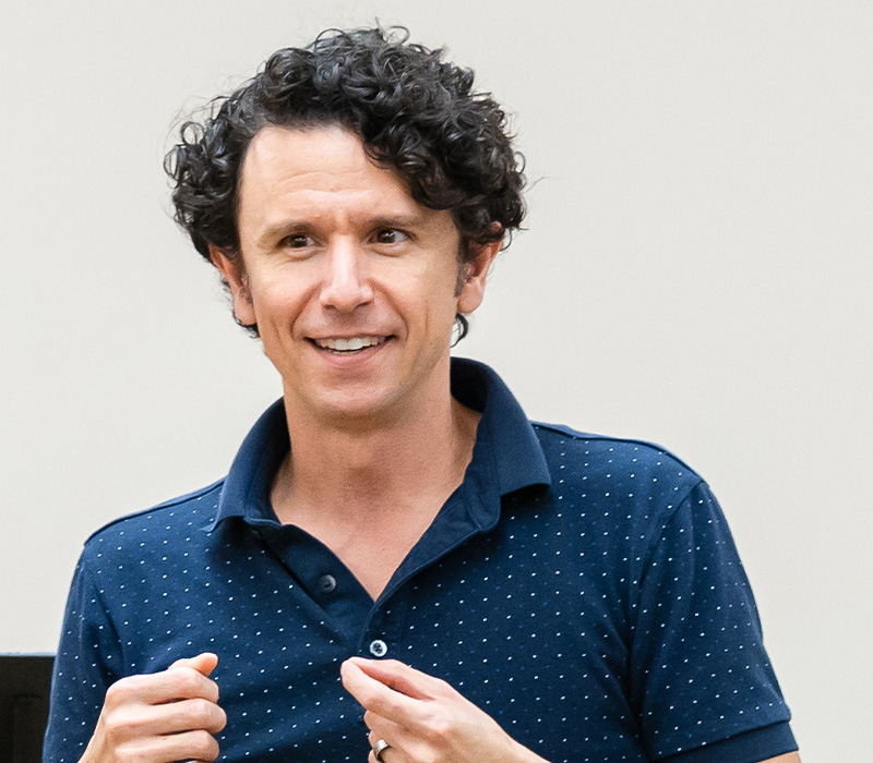 Aaron Rossini Headshot of Aaron Rossini with curly hair, wearing a navy polo shirt, photographed indoors.