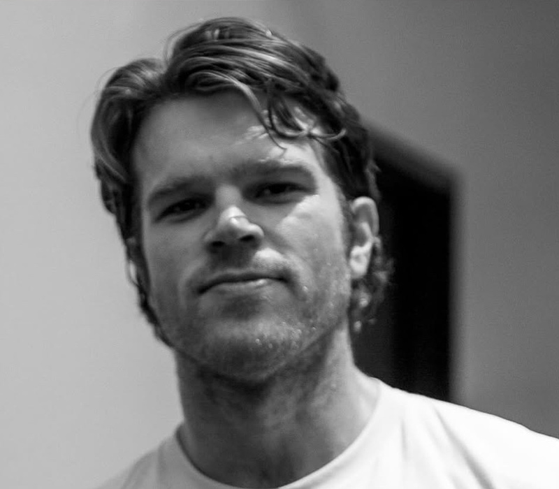 cyrus-hobbi Black-and-white headshot of an actor with short hair and light facial hair, wearing a white T-shirt.