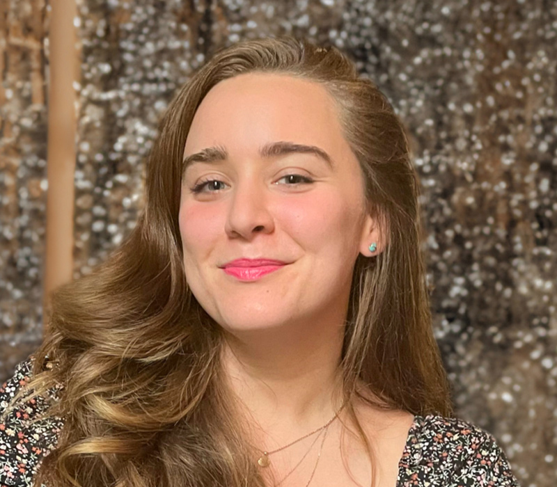 laura-winters Headshot of a smiling woman with long light brown hair, wearing a patterned top, photographed outdoors.
