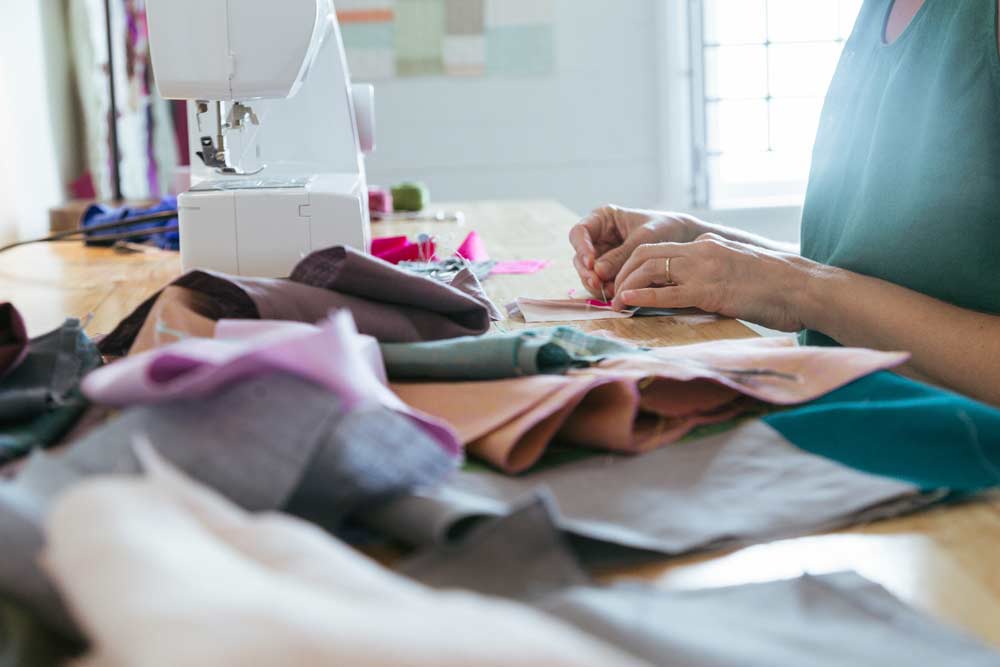 Hands sewing fabric pieces at table beside sewing machine in textile class