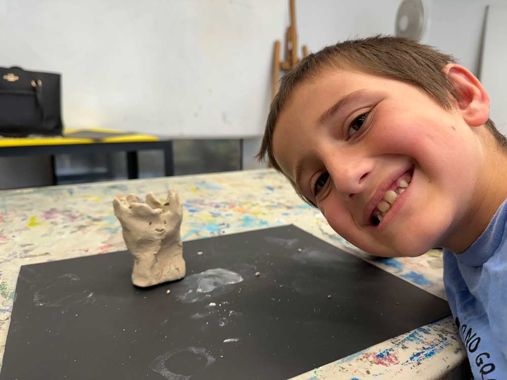 Smiling child showing small clay sculpture in hands-on art class