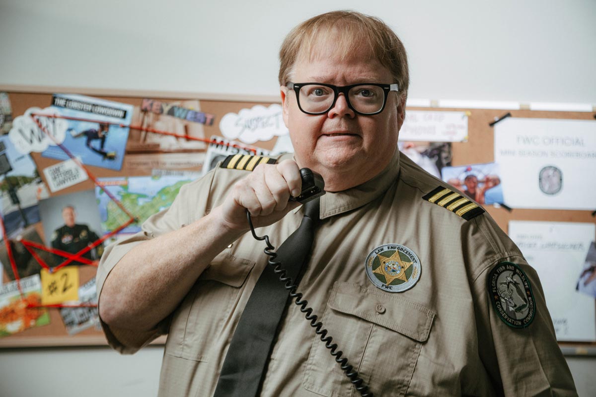 Uniformed wildlife officer speaking into radio in front of investigation board with photos and notes